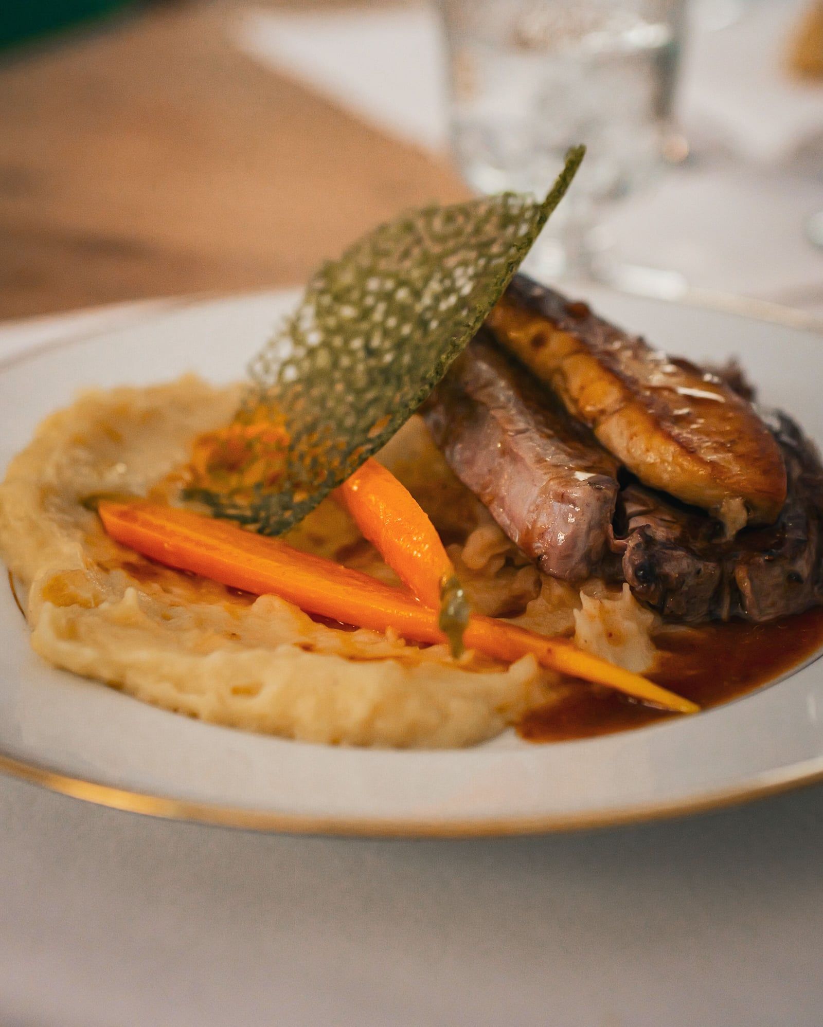 Filet de bœuf et son escalope de foie gras poêlée, mousseline de pomme de terre truffée et carottes glacées, décorée d’une tuile dentelle à la fane de carottes. Jus de viande corsé