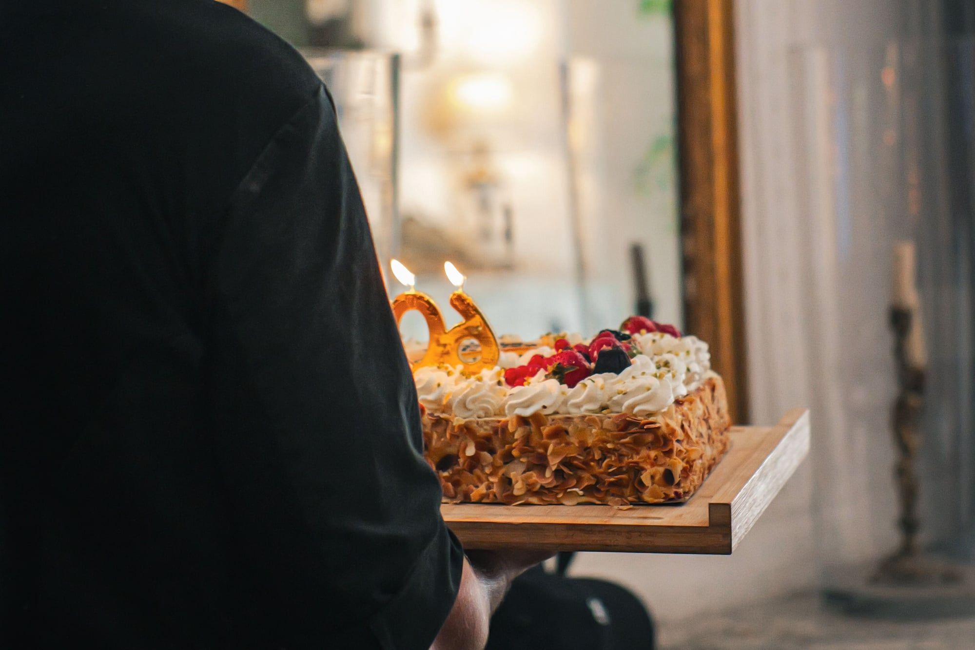 Le chef de dos portant un gâteau d'anniversaire aux bougies allumées devant un miroir doré