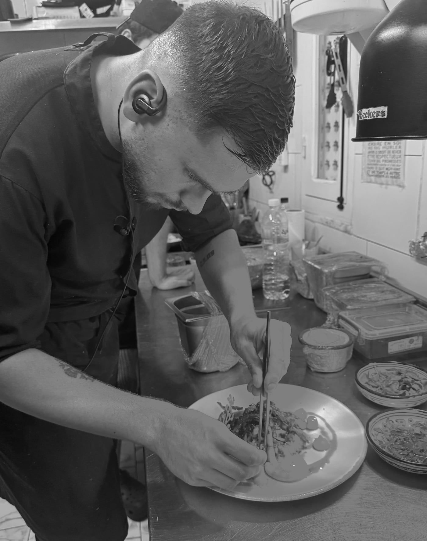 Le chef, un écouteur à l'oreille, dresse une assiette à la pince en cuisine